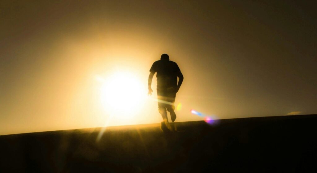Silhouette of a man running uphill against a bright desert sunrise, capturing a sense of solitude and determination.